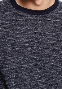Maglione blu navy con un motivo a maglia testurizzata e un colletto a girocollo a coste. Realizzato in un tessuto morbido, presenta un aspetto leggermente mélange.