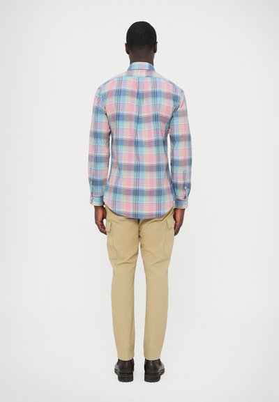 Večbarvna karo srajca z dolgimi rokavi, svetlo modrim ovratnikom in gumbi, kombinirana z bež kavbojkami in temnimi čevlji.