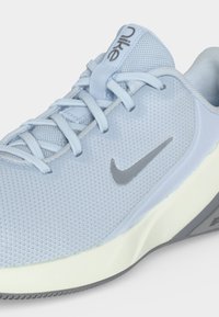 Φωτεινό γαλάζιο παπούτσι τρεξίματος Nike με άνω μέρος από δίχτυ, κορδόνια, γκρι λογότυπο swoosh και λευκή μαλακή σόλα που είναι κεκλιμένο για να δείχνει λεπτομέρειες από το πλάι και πάνω.