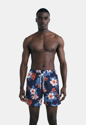 Pantaloni da bagno blu navy con motivo floreale in rosso e bianco, dotati di cintura elastica e cordoncino bianco.