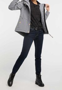 Šedá softshellová bunda se zlatými knoflíky, spárována s černým košilovým topem s puntíky, tmavě modrými skinny džínami a černými šněrovacími bojovými botami.