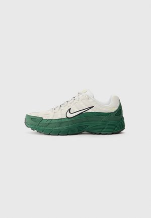 Nike sneakers featuring a cream upper with green accents, textured fabric, a black swoosh, and a patterned rubber sole. Side view.