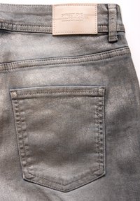 Metallisk grå denimjeans med en texturerad finish, utrustad med en enda bakficka och en läderetikett i tan vid midjan.