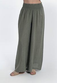 Pantaloni a gamba larga in un verde oliva tenue, realizzati in tessuto leggero con vita elastica. Abbinati a sandali piatti intrecciati.