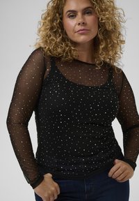 Sort langærmet top med en mesh-overlay og sølvmetallic prikker, rund halsudskæring og tætsiddende silhuet.
