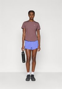 Αθλητική εμφάνιση με καφέ πουκάμισο κοντού μανικιού και ανοιχτό μπλε σορτς. Μαύρο μπουκάλι νερού και μαύρα αθλητικά παπούτσια με λευκές κάλτσες.