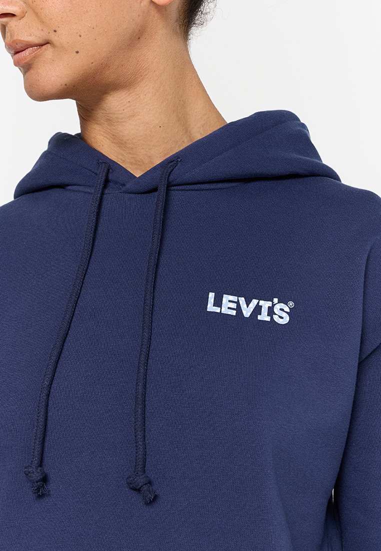 Primer plano de una persona que lleva puesta una sudadera de Levi's de color azul marino con cordones, mostrando el logo en el pecho y parte del cuello y la cara.