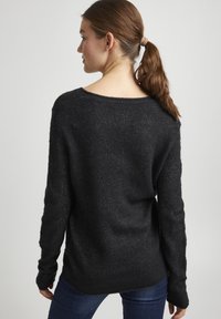 Pull en maille noir avec un décolleté large et des manches longues. Tissu texturé avec un léger éclat, présentant une coupe décontractée et un ourlet côtelé.