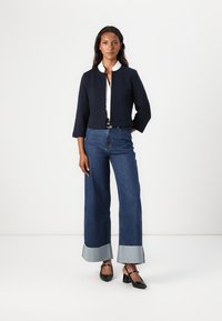 Marineblauwe kort jasje met driekwartmouwen, wit coll shirt eronder, brede denim broek met rafelrand en zwarte hakken.
