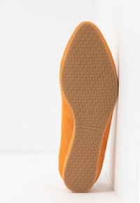Chaussure plate orange reposant sur le côté, montrant la semelle en caoutchouc texturée avec de petites grips à motifs et une indication de taille 37.