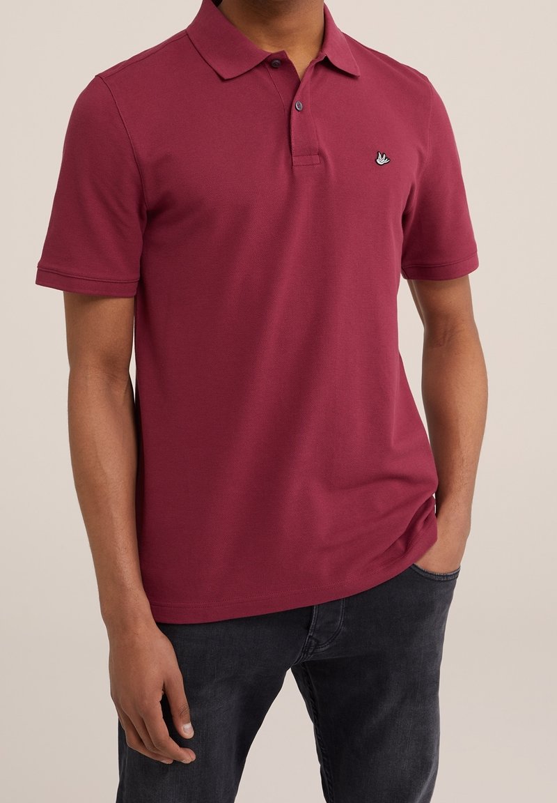 Vínová polo tričko s klasickým límečkem, krátkými rukávy a malým černým vyšívaným logem na hrudi; vyrobeno ze měkké, strukturované látky.