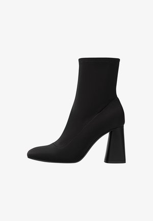 Bottine noire à design similaire à une chaussette, avec un embout pointu et un talon large. Fabriquée en tissu lisse avec des détails de couture invisibles.