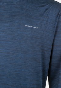 Langärmliges Sportshirt in tiefblau mit strukturiertem Muster. Besitzt ein weißes "ENDURANCE"-Logo im oberen linken Brustbereich.