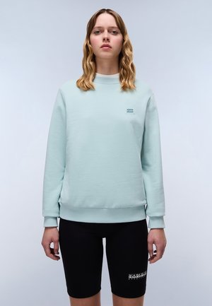 Muntgroene sweatshirt met een ronde halslijn, geribbelde boorden en zoom, gecombineerd met zwarte fietsshorts met een logodetail aan de zijkant.