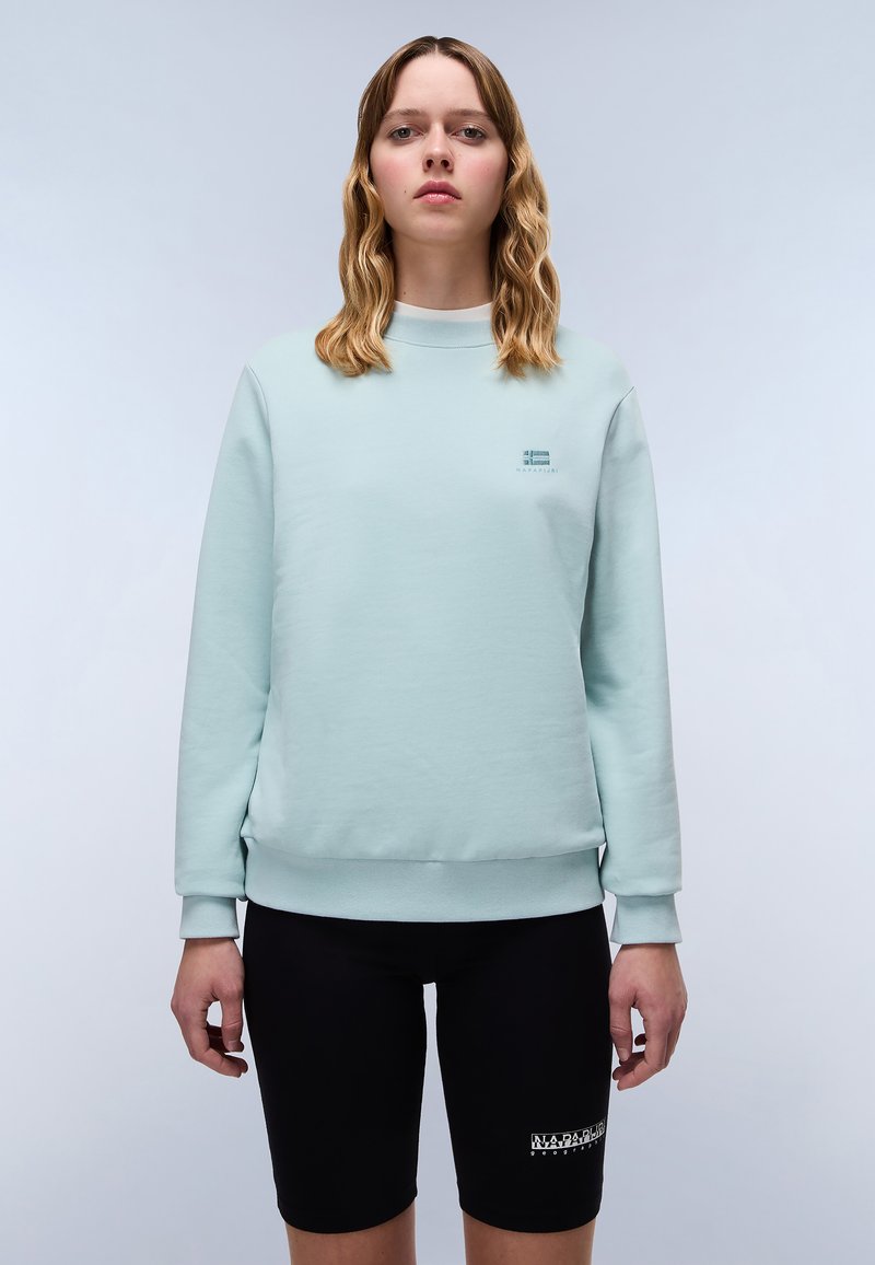 Felpa verde menta con collo a giro, polsini e orlo a costine, abbinata a pantaloni bicycle neri con dettaglio del logo sul lato.