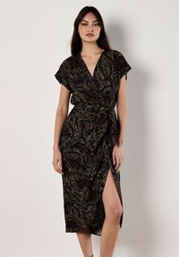 Robe noire enroulée avec un motif de feuilles en or et rouille. Manches courtes, décolleté en V profond et une fente sur le côté pour le contraste. Fabriquée en tissu léger.