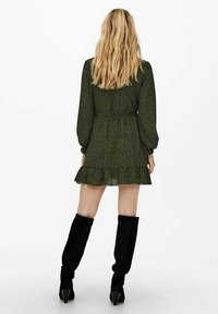 Robe fleurie verte avec manches longues bouffantes, ourlet à volants et taille cintrée. Associée à des bottes noires montant jusqu'aux genoux.