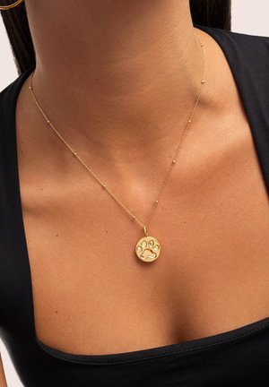 Collier en pendentif en or présentant un charme circulaire avec un design de patte, sur une chaîne délicate avec de petits accents de perles texturées.