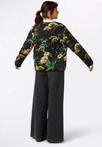 Quilted black jacket with colorful floral pattern, featuring long sleeves, a relaxed fit, and a round neckline. Paired with black wide-leg pants.