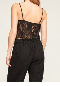 Svart spetscroptop med tunna axelband, med en genomskinlig design och blommönster på baksidan, tillsammans med svarta elastiska spetsbyxor.