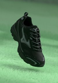 Fekete sportcipő texturált szövetből, fényvisszaverő részletekkel és ívelt formával. Szürke fűzőkkel és könnyű húzást segítő füllel rendelkezik.