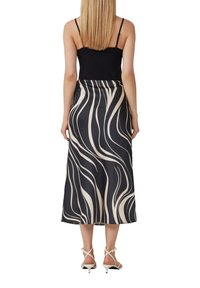 Zijde midi rok in zwart en crème met golfpatroon, voorzien van een elastische tailleband en een gladde, glanzende textuur. Witte sandaaltjes met banden complementeren de look.