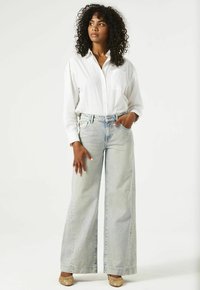Witte overhemd met knopen, ontspannen wijd-zittende lichtblauwe denim jeans met een zakdetail, accentuerend met gevlochten tan schoenen.