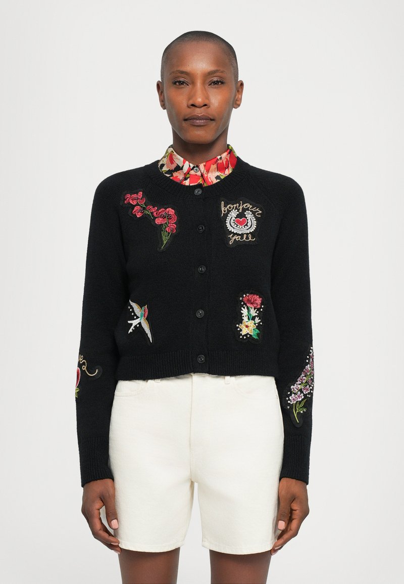 Black cropped cardigan with floral embroidery in red, white, and green designs, featuring button front and ribbed cuffs with detailed accents.