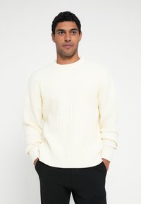 Roomkleurige trui in een gestructureerde breiwerk, met een ronde halslijn en geribbelde manchetten en zoom, gecombineerd met donkere broek.