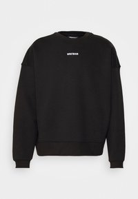 Sweat-shirt noir à col rond avec manches longues et petit texte blanc « WRSTBHVR » centré sur la poitrine.