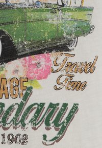 Gráfico de un coche vintage verde sobre un tejido claro, con acentos florales coloridos y texto que dice "Tiempo de Viaje" y "Legendario 1962".