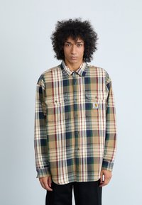 Camisa de cuadros en colores beige, verde y burdeos, confeccionada en tejido texturizado, con cuello clásico y dos bolsillos frontales.