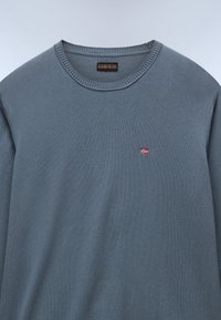 Grijze crewnecktrui van zachte stof. Bevat een klein Noors vlagembleem op de borst. Geribde boorden en halslijn.