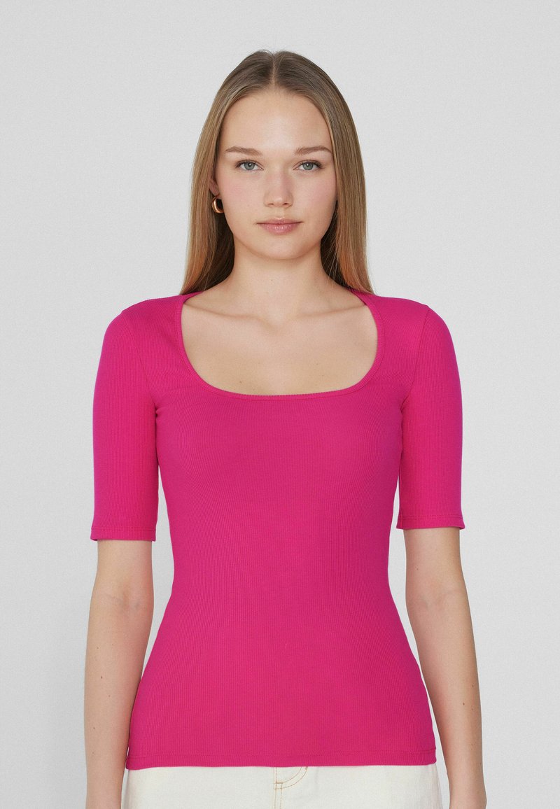Top ajustado de manga corta y canalé en rosa brillante, con escote cuadrado y textura suave, combinado con prendas de parte inferior de color claro.