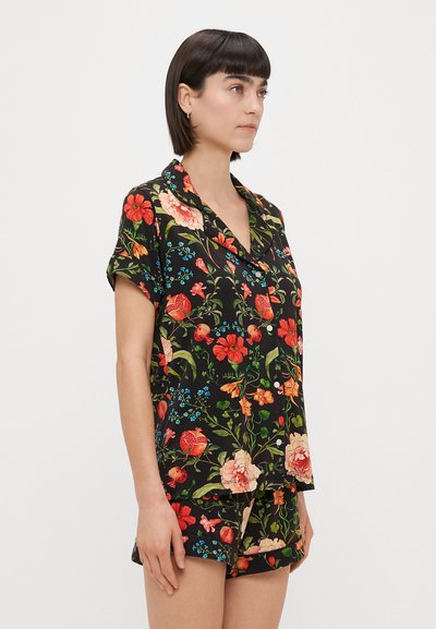 Conjunto de pijama floral com mangas curtas e calções, feito de tecido leve. Fundo preto com padrões florais vibrantes em vermelho, rosa e azul.