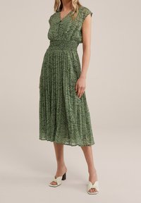 Vestito midi verde con scollatura a V, vita arricciata, maniche a cappuccio e motivo a foglie. Abbinato a décolleté leggere verde chiaro.