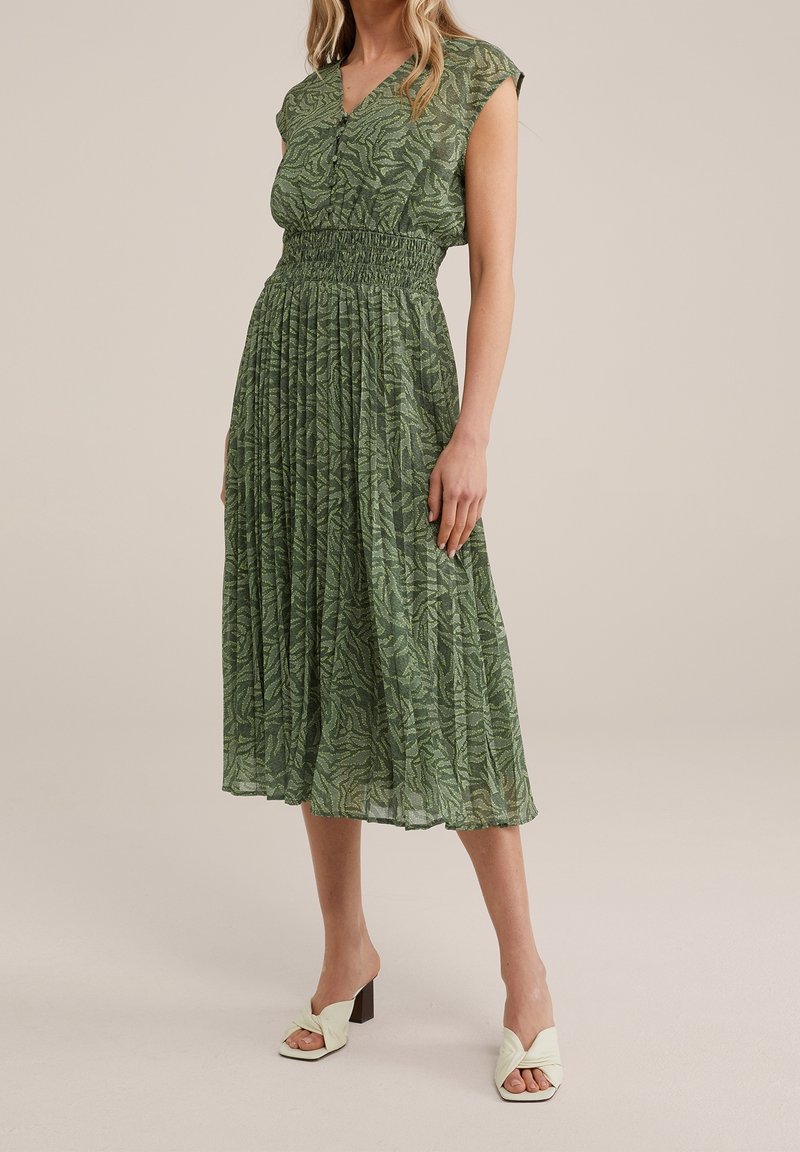 Vestito midi verde con scollatura a V, vita arricciata, maniche a cappuccio e motivo a foglie. Abbinato a décolleté leggere verde chiaro.
