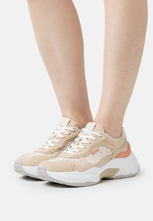 Baskets en daim beige et en mesh avec des lacets blancs, logo BOSS orange et semelle blanche épaisse portées pieds nus.