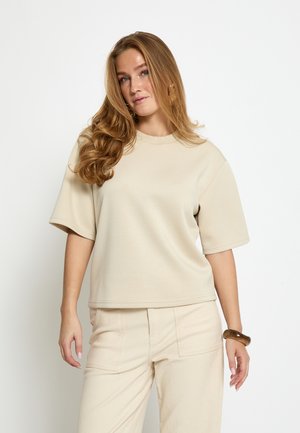 Beige kortærmet top i blødt materiale med afslappet pasform og rund halsudskæring. Kombinationen er med lysebeige, vidde bukser.