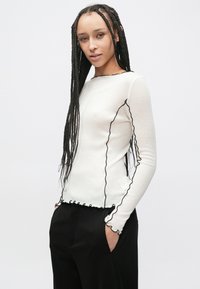 Bluză cu mâneci lungi din bumbac crem, cu margini negre în formă de val pe decolteu și manșete, cu croială strâmtă și textură moale.