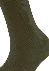 Chaussette vert olive avec un motif en chevrons texturé. Fabriquée en tissu tricoté, elle présente une finition lisse et une forme effilée.