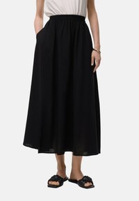 Gonna lunga nera con vita elastica e tasche laterali, realizzata in tessuto leggero con una vestibilità fluida e morbida. Nessun motivo visibile o accessori.