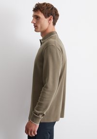 Olivgrünes Langarm-Polohemd mit geripptem Kragen, das über einen dezenten weißen Saum und einen lässigen Schnitt verfügt. Sanfte Baumwolltextur.
