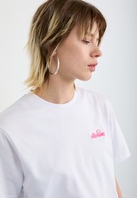 T-shirt en coton blanc avec un logo brodé rose. Conçu avec un col rond et des manches courtes, offrant une coupe régulière.