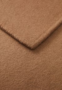 Brun filtstoff med en teksturert overflate, som har to overlappende lag: ett som er litt hevet med en glatt kant og en lodden finish.