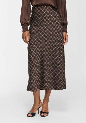 Falda midi marrón con estampado, combinada con blusa marrón de manga larga y zapatos de tacón altos negros con puntera abierta sobre un fondo claro.