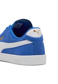Sneaker blu in suede con accenti in pelle bianca, suola piatta in gomma bianca e logo dorato sul tallone. I dettagli del cucito a vista aumentano la texture.