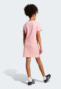 Rózsaszín, bordázott ruházat rövid ujjakkal, a térd fölé érve. Tengerészkék és rózsaszín sportcipővel párosítva, fehér bokazoknival.