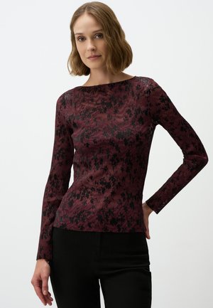 Langarmshirt in kastanjebruin met een gestructureerd zwart patroon, voorzien van een bootnek en een fitted silhouet. Draagt met zwarte broek.
