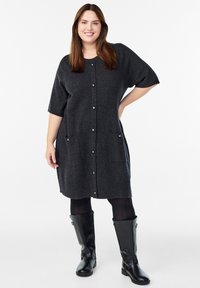 Tamsiai pilka megzta suknelė trumpomis rankovėmis, su sagų uždarymu ir dviem priekinėmis kišenėmis. Dėvima ant juodų pėdkelnių ir ilgų odinių batų.